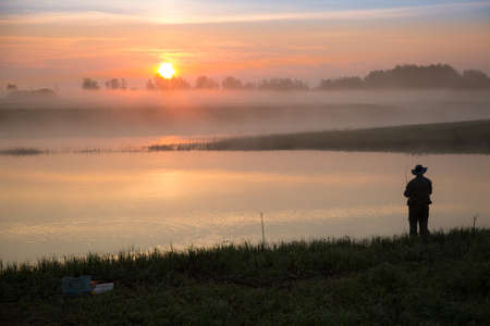 A spinner is catching a pike on the river at sunriseの写真素材