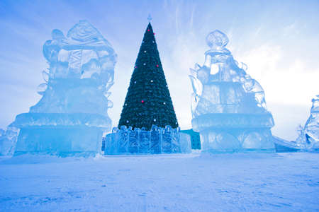A Christmas tree stands on an ice town between two ice figuresの写真素材