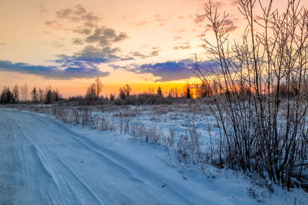 Winter road laid along the floodplain of the river against the background of the setting sun