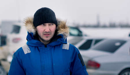 Young man in a blue down jacket against a car backgroundの写真素材