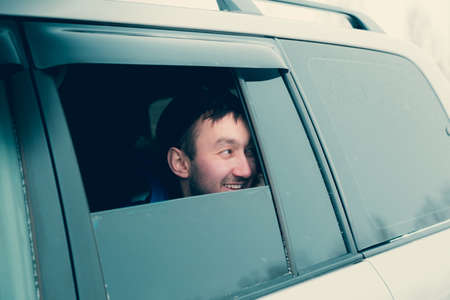 A young man looks out of an open window of an SUV carの写真素材
