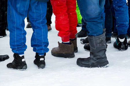 People shod in different winter shoes against the background of snowの写真素材
