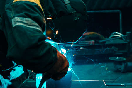 A welder welds a metal piece and sparks from welding fly in different directionsの写真素材