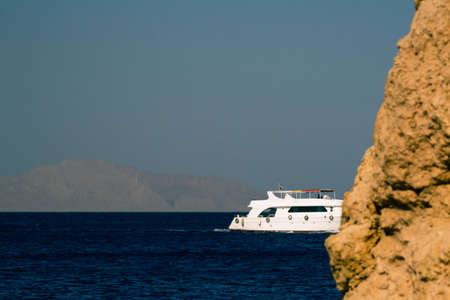 Snow-white pleasure yacht hides from the view of the coastal rock against the backdrop of the islandの写真素材