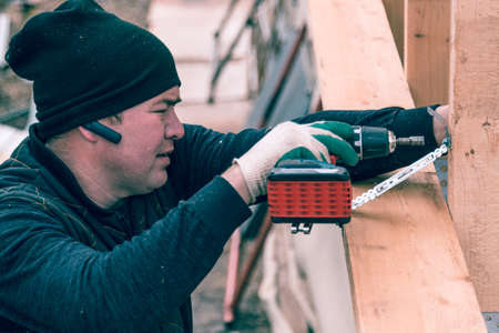 A man screws a screwdriver with an electric screwdriver into a wooden boardの写真素材
