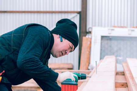 A man screws a screwdriver with an electric screwdriver into a wooden boardの写真素材