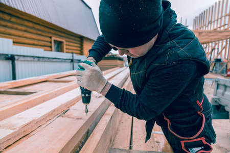 A man screws a screwdriver with an electric screwdriver into a wooden board
