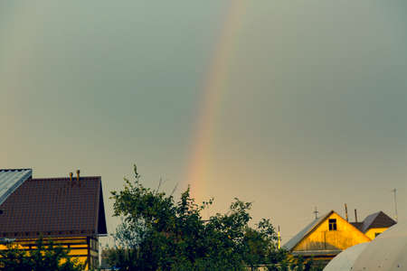 Rainbow after the rain on the blue sky over the roofs of the housesの写真素材