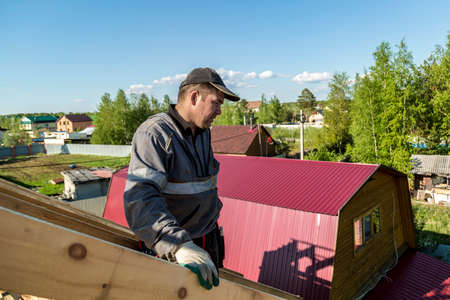 The builder stands on the roof of a wooden house and thinks how to put transverse lags