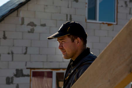 The builder stands on the roof of a wooden house and thinks how to put transverse lagsの写真素材