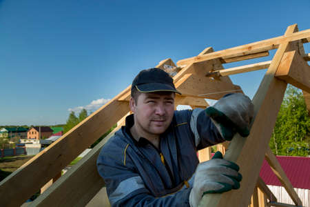 The builder stands on the roof of a wooden house and thinks how to put transverse lags