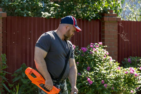 A man mowing grass on a lawn near a fence with a lawn mower