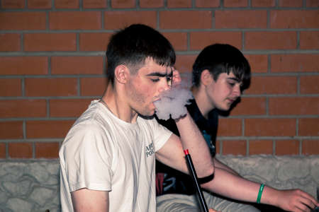 A guy smoking a hookah against a brick wall background
