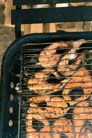 Steaks from fresh salmon are cooked on charcoal in a barbecue on the background of birch logs
