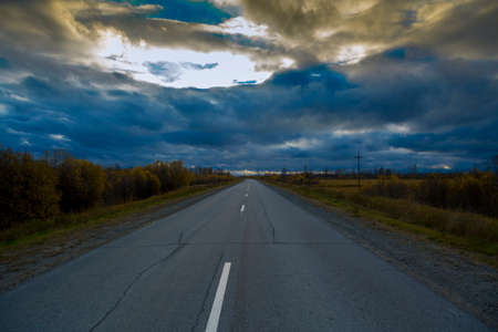 Deciduous autumn forest grows along an asphalt road with a discontinuous divided strip against the...