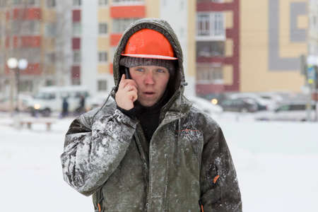 Portrait of an assembler worker in a hooded jacket talking on a mobile phoneの写真素材