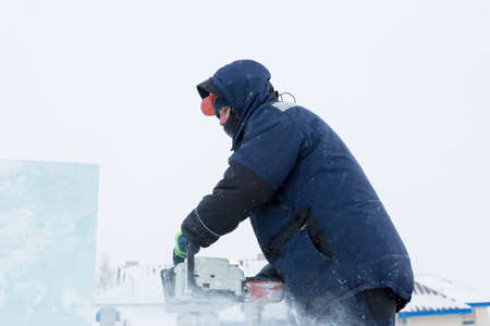 Construction worker saws an ice plate with a chainsaw