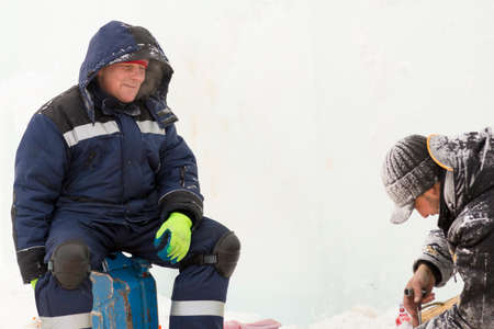 Worker in winter overalls checks the chainsaw chain on a sheet of plywood