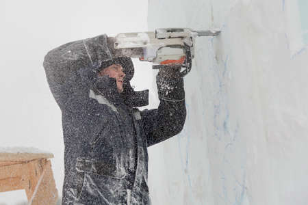 The sculptor cuts an ice figure out of ice by a chainsaw for Christmasの写真素材