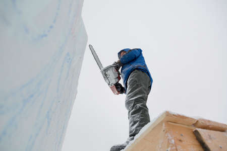 The sculptor cuts an ice figure out of ice by a chainsaw for Christmas