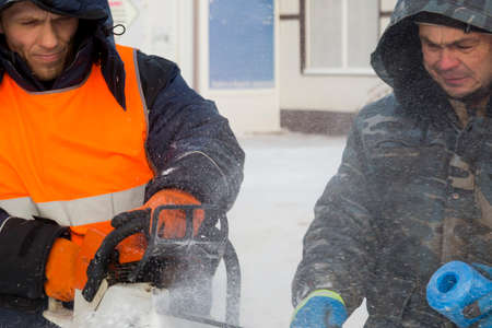 Worker installer in orange reflective vest chainsaw sets ice plateの写真素材