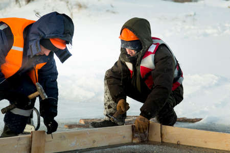 Installers in winter overalls collect formwork for an ice hole from boards