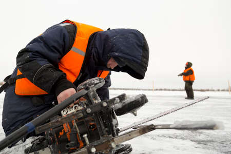An ice sawyer repairs a saw on the ice of a frozen lake at low temperature in extreme conditions