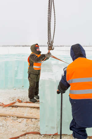 Worker slinger in orange reflective vest and helmet unloads ice panels