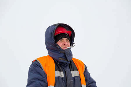 Portrait of a worker in a blue jacket with a hood on his head and a cigarette in his mouth