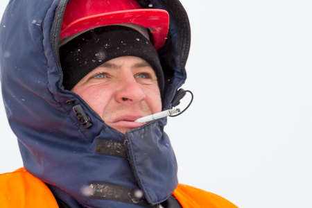Portrait of a worker in a blue jacket with a hood on his head and a cigarette in his mouth