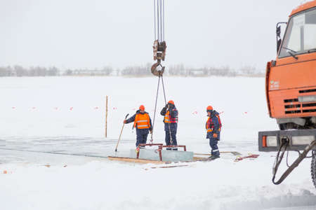 Workers observe the lifting of ice plates with a lane crane using metal frames