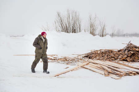 An installer in green winter workwear walks along an assembly site against a background of stacked...