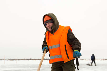 Worker on the ice of a frozen lake with bogr in his hand on ice mining