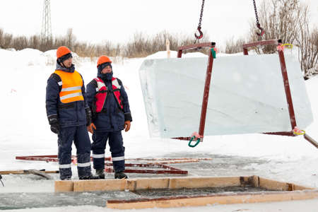 Workers observe the lifting of ice plates with a lane crane using metal frames