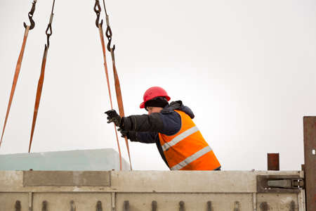 Worker slinger in orange reflective vest and helmet unloads ice panels