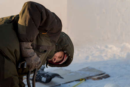 A worker pulls an ice block out of the hole with steel tongs.