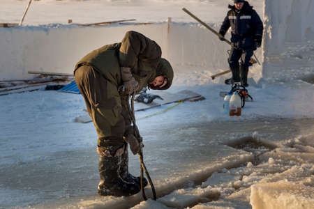 A worker pulls an ice block out of the hole with steel tongs.