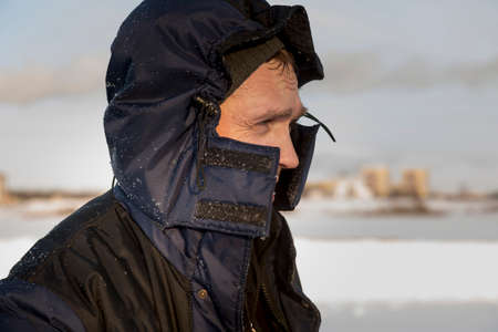 Portrait of a builder at the workplace in a winter suit, with a hood on his head