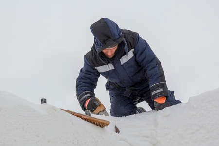Builder with a hacksaw in his hand on a snow plate in a blue jacket with a hood on his head