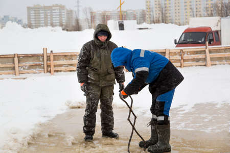 Worker with iron tongs captures on the ice of a frozen riverの写真素材