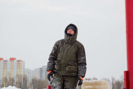 An installer in a green jacket with a hood on his head on the ice of a frozen riverの写真素材