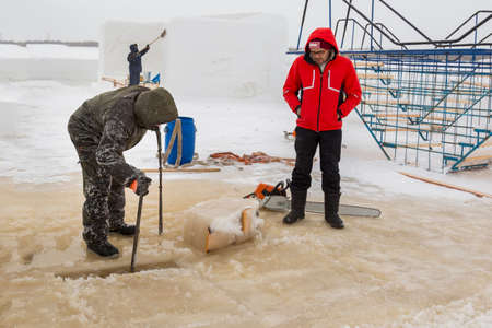 Installers in winter overalls are talking on the ice of a frozen river