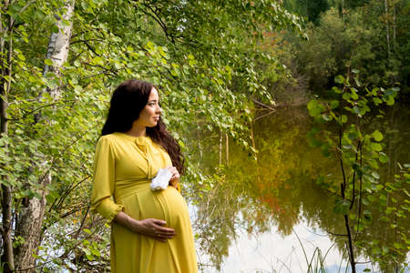 Portrait of a pregnant woman in a yellow dress in the autumn forestの写真素材