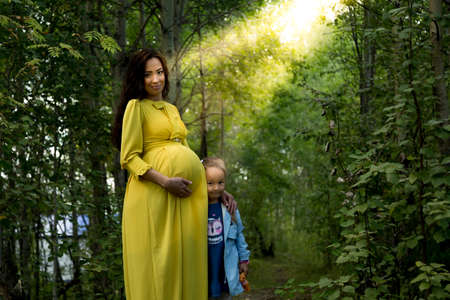 Portrait of a pregnant woman in a yellow dress with her daughter in the autumn forest