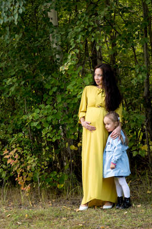 Portrait of a pregnant woman in a yellow dress with her daughter in the autumn forestの写真素材