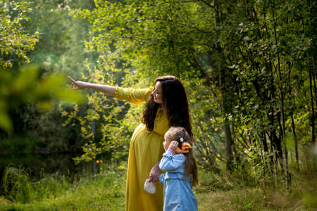 Portrait of a pregnant woman in a yellow dress with her daughter in the autumn forestの写真素材