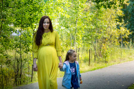 Portrait of a pregnant woman in a yellow dress with her daughter in the autumn forestの写真素材