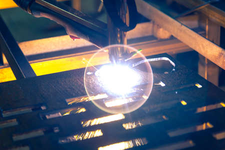 Plasma cutting machine burns through a thick sheet of steel by scattering drops of molten metal in...
