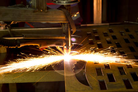 Plasma cutting machine burns through a thick sheet of steel by scattering drops of molten metal in...