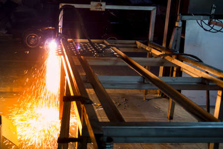 Plasma cutting machine burns through a thick sheet of steel by scattering drops of molten metal in...